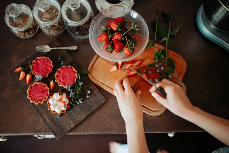 a close up of a person cutting food on a cutting board, a still life, by Julia Pishtar, pexels contest winner, made of flowers and berries, sitting on a mocha-colored table, strawberries, crafts and souvenirs