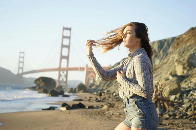 a beautiful young woman standing on top of a sandy beach, by Marshall Arisman, pexels contest winner, happening, golden gate bridge, mid - length hair, profile image, youtube thumbnail