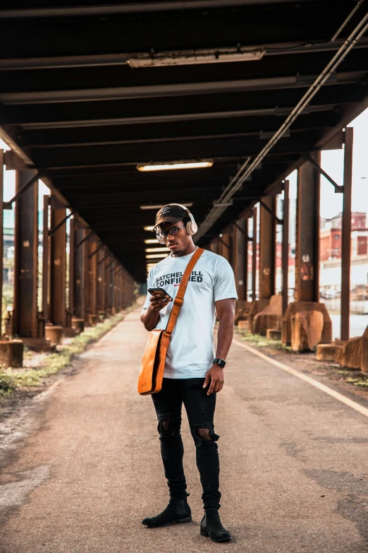 a man standing on the side of a road, by Robbie Trevino, trending on unsplash, graffiti, handsome hip hop young black man, pewdiepie selfie at a bridge, graphic tees, pittsburgh