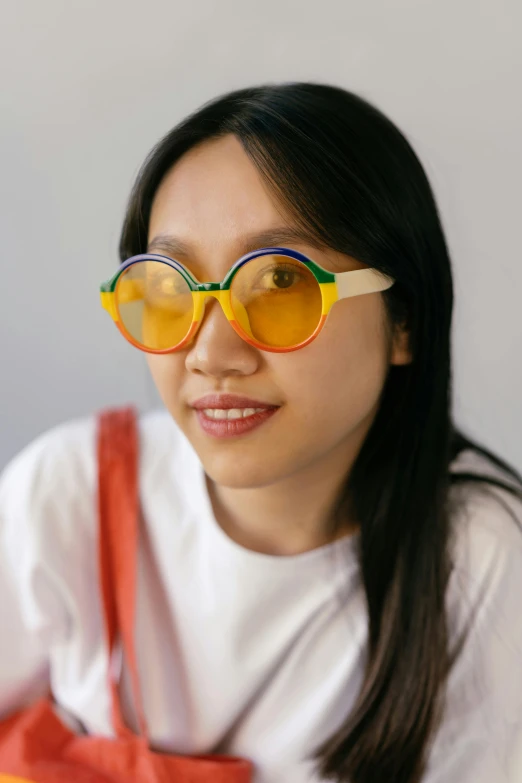 a woman wearing sunglasses and a tote bag, inspired by Gao Cen, unsplash, visual art, primary colours, circular glasses, gradient yellow, south east asian with round face