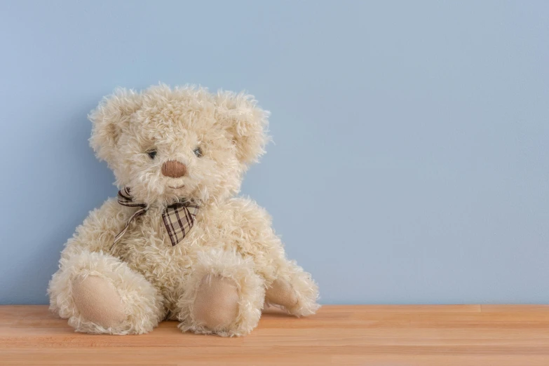 a teddy bear sitting on top of a wooden table, pale blue, background image