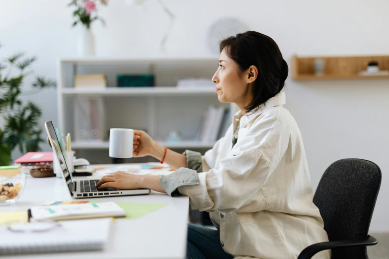 a woman sitting at a desk with a laptop and a cup of coffee, profile image