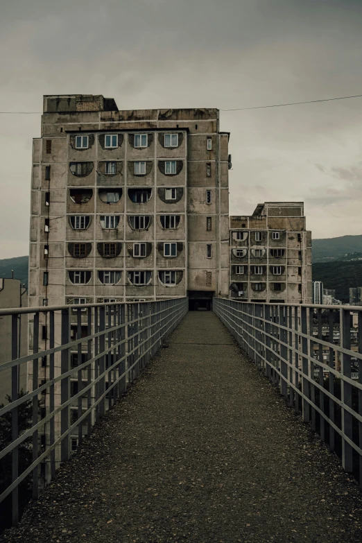 a bridge over a body of water with a building in the background, inspired by Elsa Bleda, unsplash contest winner, brutalism, ground level view of soviet town, highrise made up staircases, creepy skies, ukraine. photography