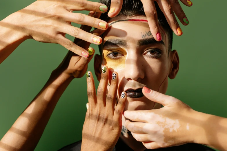 a man putting gold paint on his face, an album cover, trending on pexels, neat nails, green colored skin, non binary model, middle eastern skin