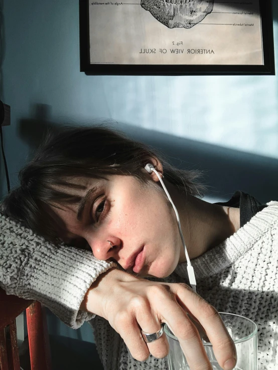 a woman sitting at a table with a glass of water, an album cover, inspired by Elsa Bleda, trending on pexels, sleepy expression, headphones, 🤤 girl portrait, portrait of depressed teen