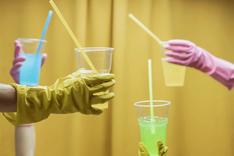 a close up of a person holding a cup of liquid, by Nathalie Rattner, pexels, plasticien, yellow latex gloves, people drink cocktails, iridescent tubes, indoor scene