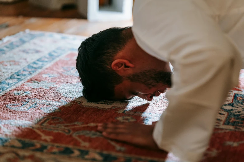 a man is doing a handstand on a rug, by Carey Morris, pexels contest winner, hurufiyya, kneeling in prayer, indoor picture, hand over mouth, muslim