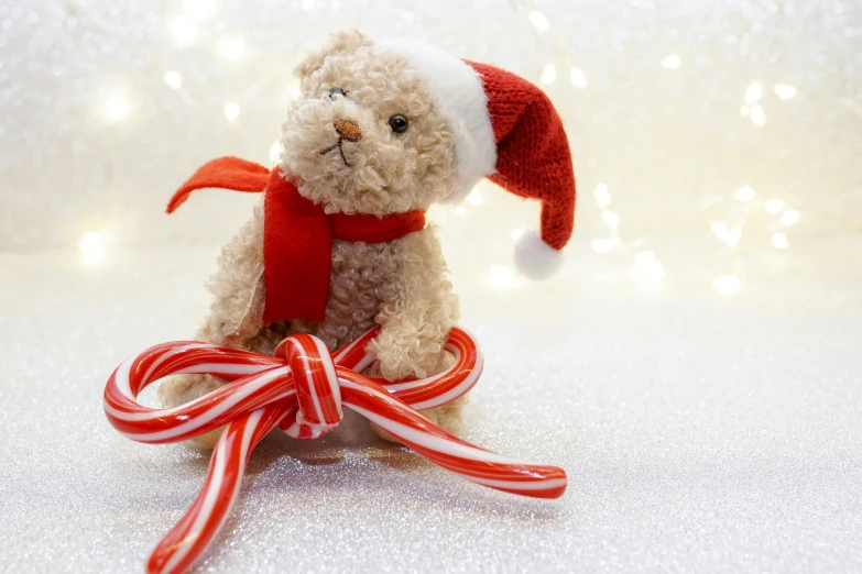 a teddy bear wearing a santa hat and holding a candy cane, by Elaine Hamilton, pexels, miniature product photo, low detail, game, laying teddy bear