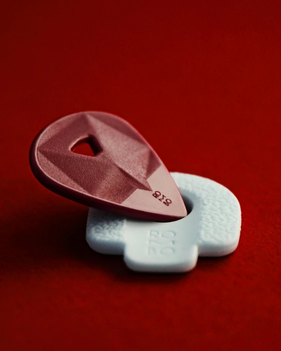 a close up of a plastic object on a red surface, contracept, non-binary, maroon and white, heartstone