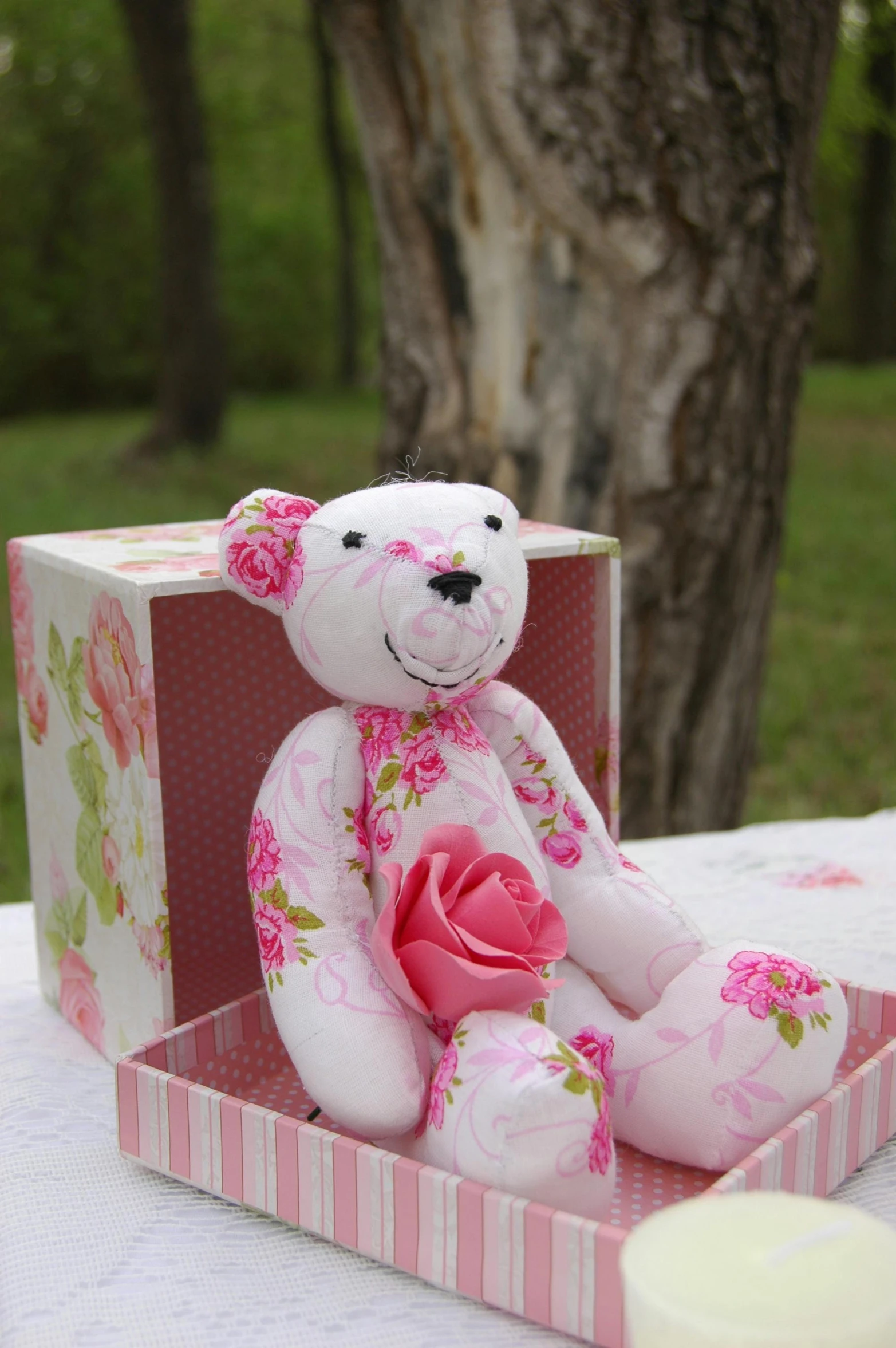 a teddy bear sitting in a box on a table, inspired by Annabel Kidston, decorative roses, pattern, pink, white