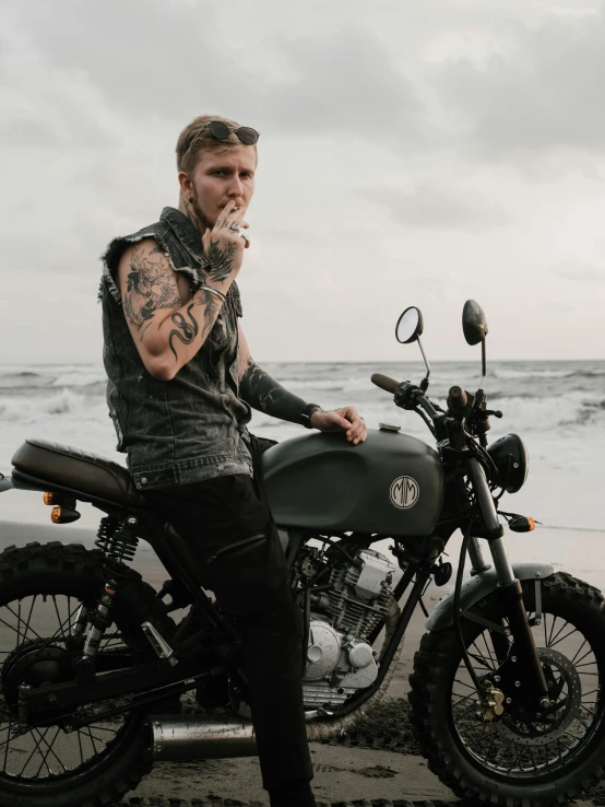 a man sitting on a motorcycle on the beach, a tattoo, inspired by Seb McKinnon, trending on pexels, drinking, sideburns, profile image, dieselpunk look