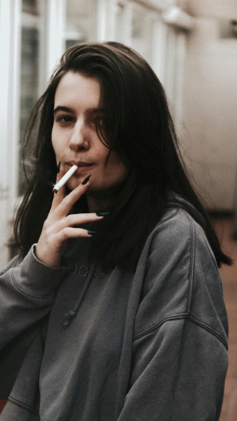 a woman with long hair smoking a cigarette, inspired by Elsa Bleda, pexels contest winner, wearing sweatshirt, woman with black hair, androgynous person, wearing casual clothing