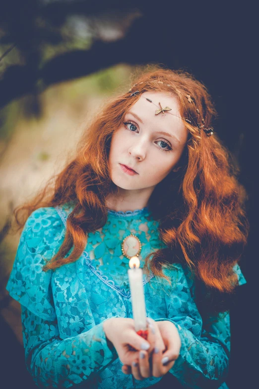 a woman in a blue dress holding a candle, inspired by Arthur Hughes, pexels contest winner, ginger wavy hair, teen elf girl, amy sol in the style of, looking towards camera