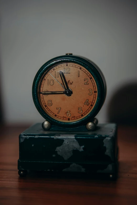 a clock sitting on top of a wooden table, an album cover, by Jessie Algie, unsplash, modernism, 1940s photo, alarm clock, mini model, historical event