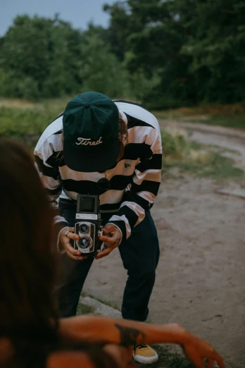 a man taking a picture of a woman with a camera, unsplash contest winner, visual art, wearing a baseball cap backwards, looking down on the camera, low quality photo, outdoor photo