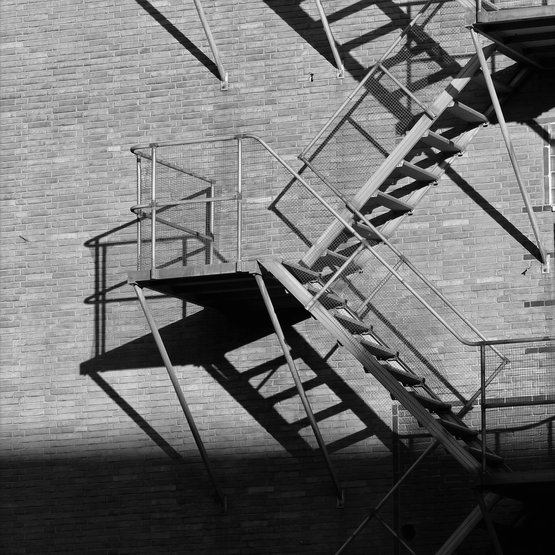 a black and white photo of a fire escape ladder, caustics shadows, square lines, penrose stairs, brick