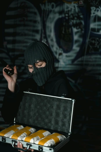 a man in a mask holding a case of beer, an album cover, trending on pexels, graffiti, man steal computers, black hood, smoking gun, crazy hacker girl