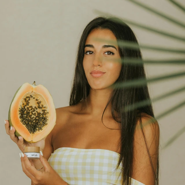 a woman holding a slice of papana in front of her face, a colorized photo, by Olivia Peguero, pexels contest winner, wearing a melon, tanned ameera al taweel, photoshoot for skincare brand, female with long black hair