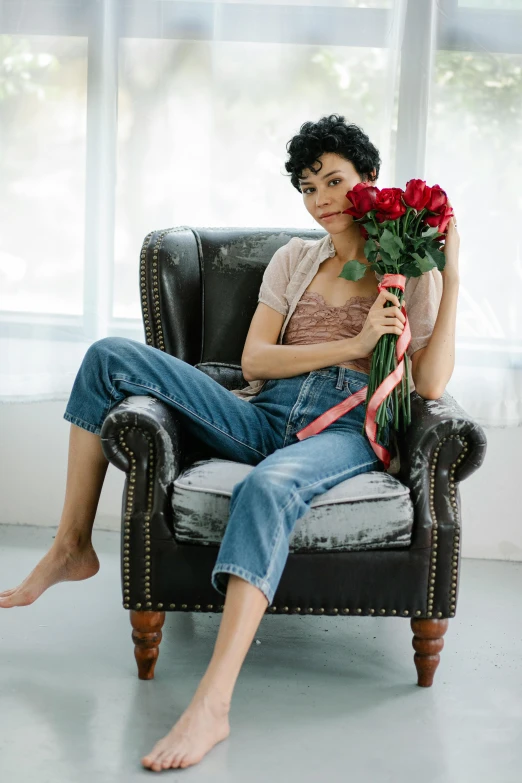 a woman sitting in a chair holding a bouquet of roses, wearing blue jean overalls, curly pixie cut hair, morena baccarin, curated collections