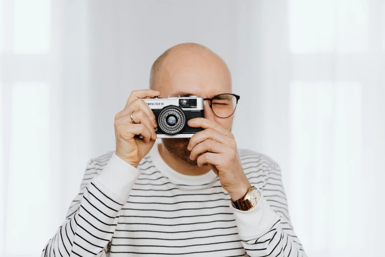 a man taking a picture with a camera, a picture, inspired by Leo Leuppi, unsplash contest winner, photorealism, wearing black rimmed glasses, in front of white back drop, radoslav svrzikapa, small glasses