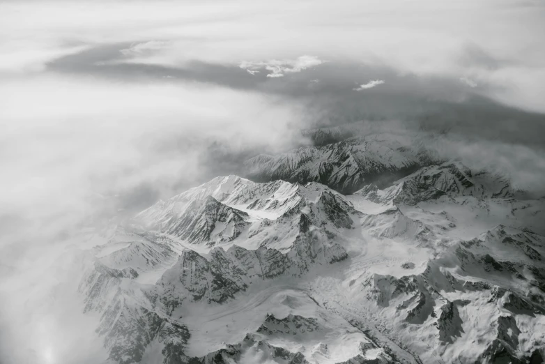 a black and white photo of a snow covered mountain, view from the sky, grayscale photography, under a gray foggy sky, airplane view