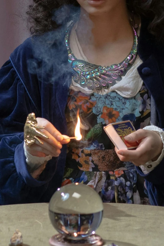 a woman sitting at a table with a lighter in her hand, inspired by Limbourg brothers, trending on pexels, dressed as an oracle, séance, photographed for reuters, gold and indigo