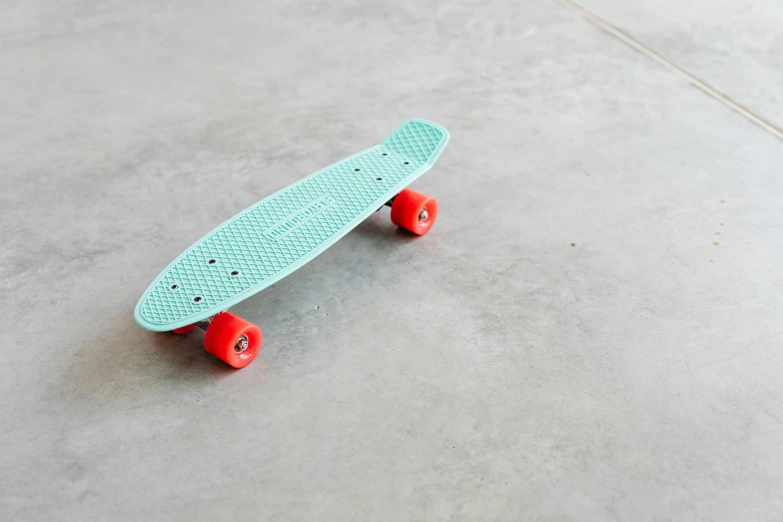 a skateboard sitting on top of a cement floor, turquoise, small, image