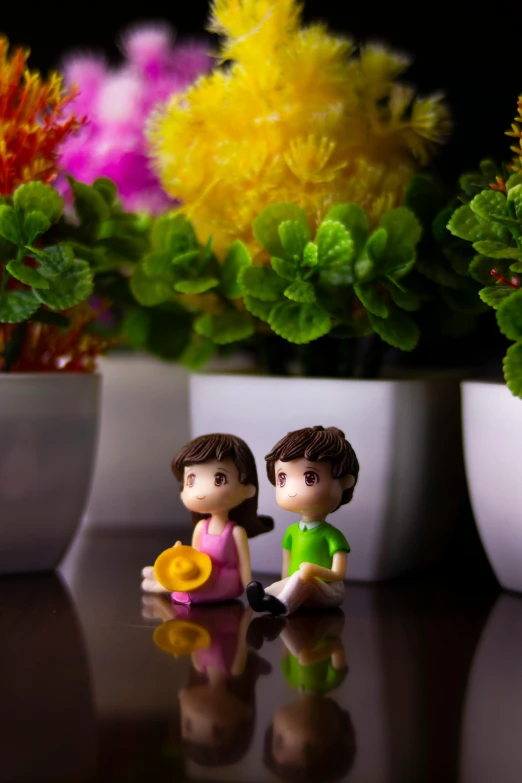 a couple of figurines sitting on top of a table, by Lilia Alvarado, with colorful flowers and plants, 35mm of a very cute, a brightly colored, anime pvc figure