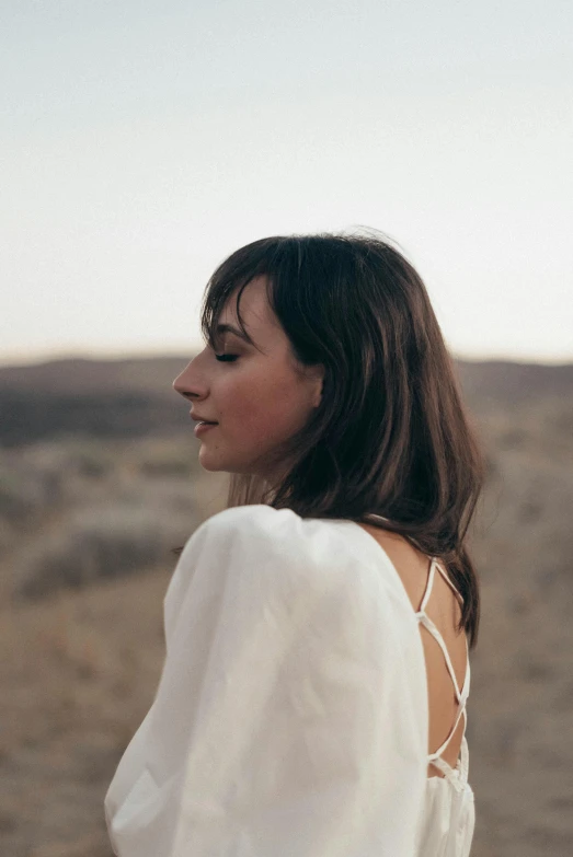 a woman in a white dress standing in the desert, an album cover, inspired by Zoë Mozert, head and shoulders view, side portrait rugged girl, girlboss, white sleeves