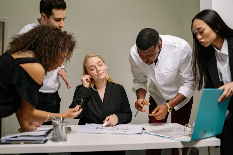 a group of people standing around a table, sitting on a desk, professional modeling, varying ethnicities, unsplash contest winning photo