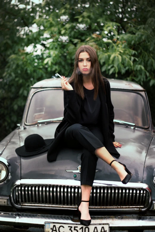 a woman sitting on top of a car smoking a cigarette, by Lucia Peka, pexels contest winner, auto-destructive art, wearing causal black suits, portrait emily ratajkowski, instagram picture, orthodox