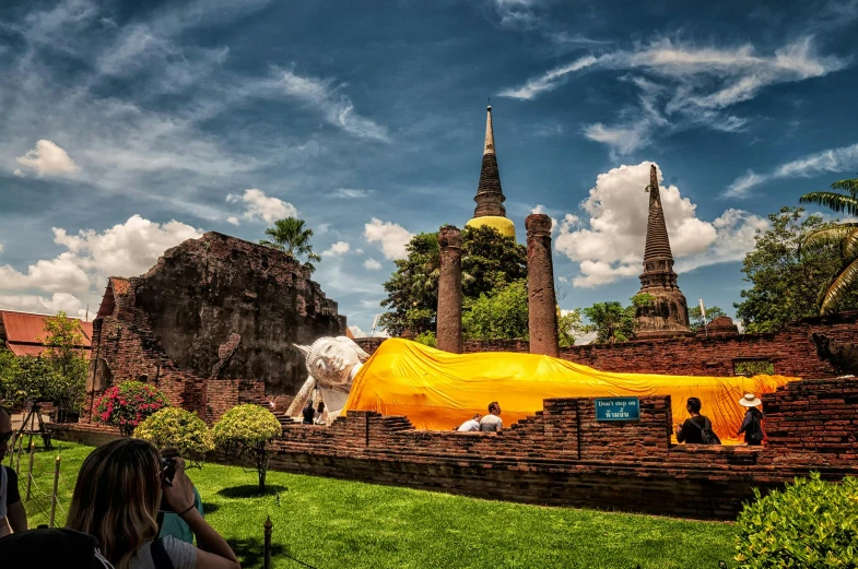 a group of people sitting on top of a lush green field, thai architecture, cathedrals and abbeys, yellow, preserved historical