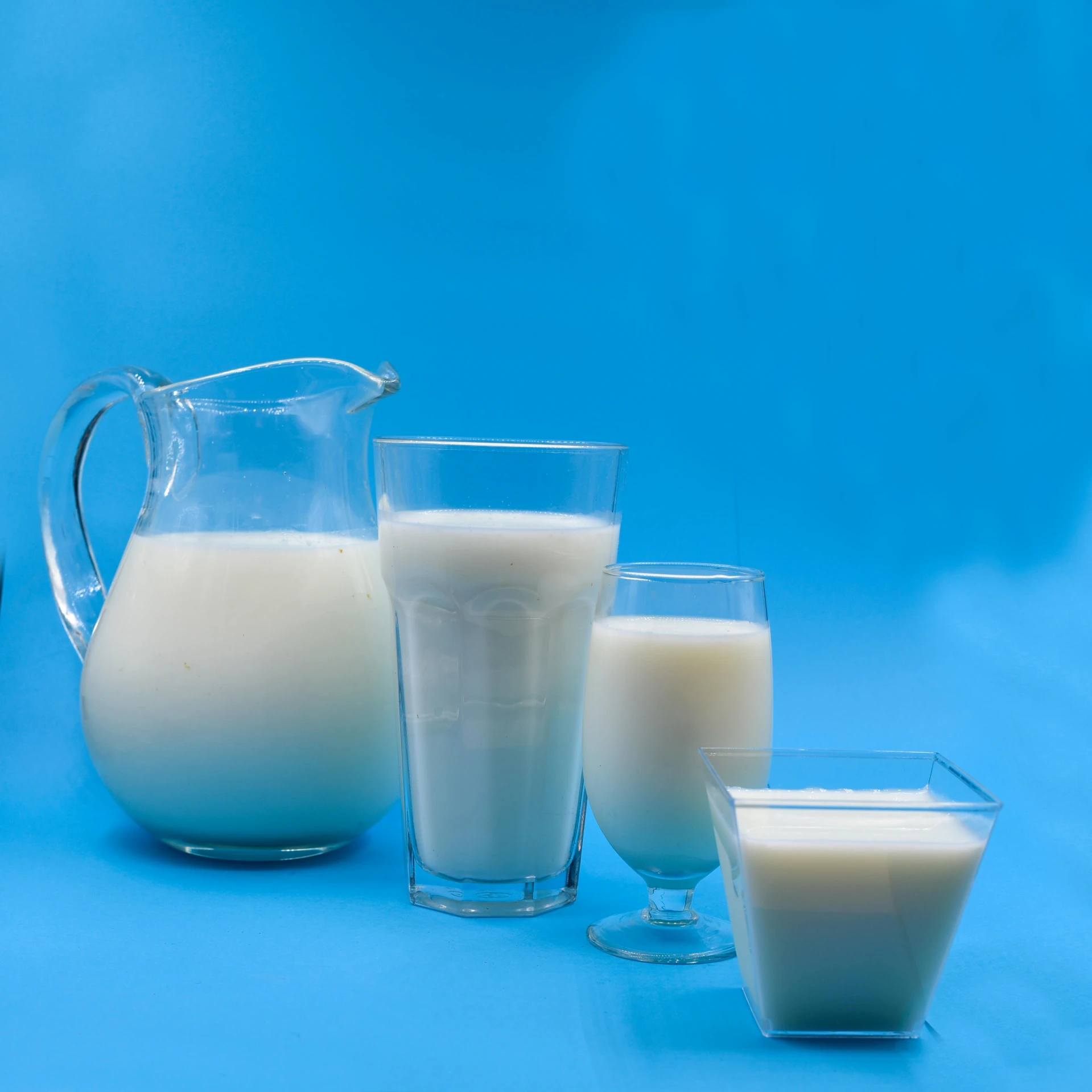 a pitcher of milk and three glasses of milk, with a blue background, ivory skin, family dinner, collection product