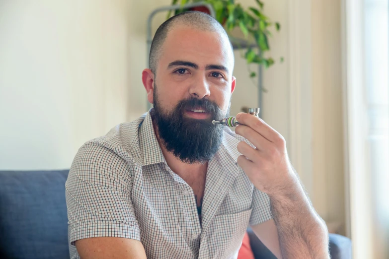 a man sitting on a couch eating a piece of food, a portrait, inspired by Constantine Andreou, pexels contest winner, hurufiyya, holding a small vape, avatar image, shaved beard, professional profile picture