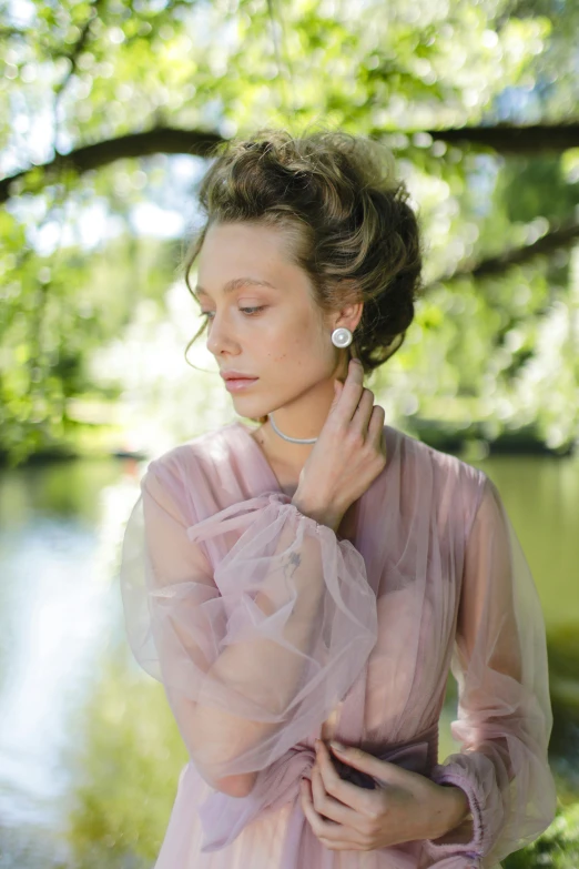 a woman standing next to a body of water, a portrait, inspired by Pierre-Joseph Redouté, pexels, rococo, thin round earrings, in a park, sydney sweeney, wearing organza gown