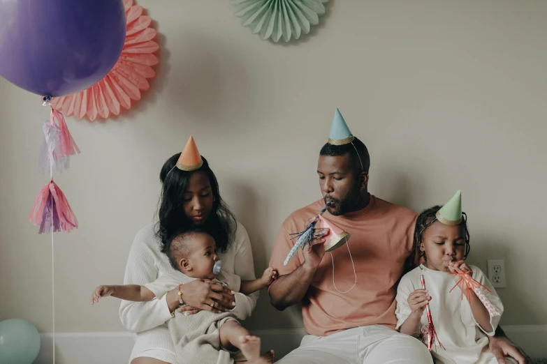 a group of people sitting on top of a bed, by Carey Morris, pexels contest winner, black arts movement, wearing a party hat, father with child, portrait featured on unsplash, party balloons