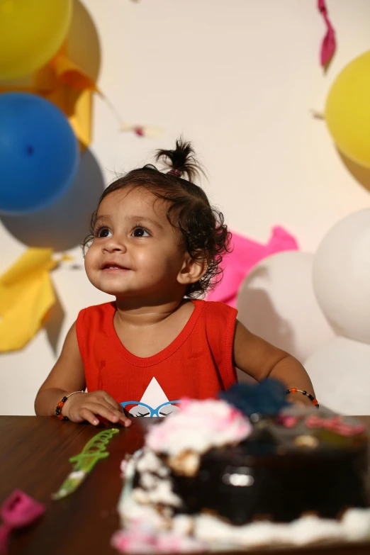 a little girl sitting at a table in front of a cake, pexels contest winner, party balloons, indian girl with brown skin, 15081959 21121991 01012000 4k, a still of a happy