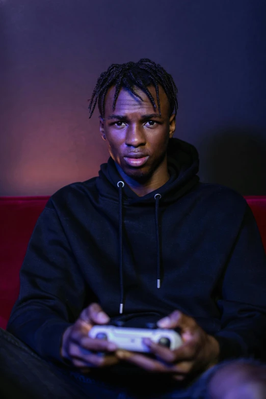 a man sitting on a couch holding a video game controller, an album cover, pexels contest winner, playboi carti portrait, dramatic lighting; 4k 8k, soccer, intense expression