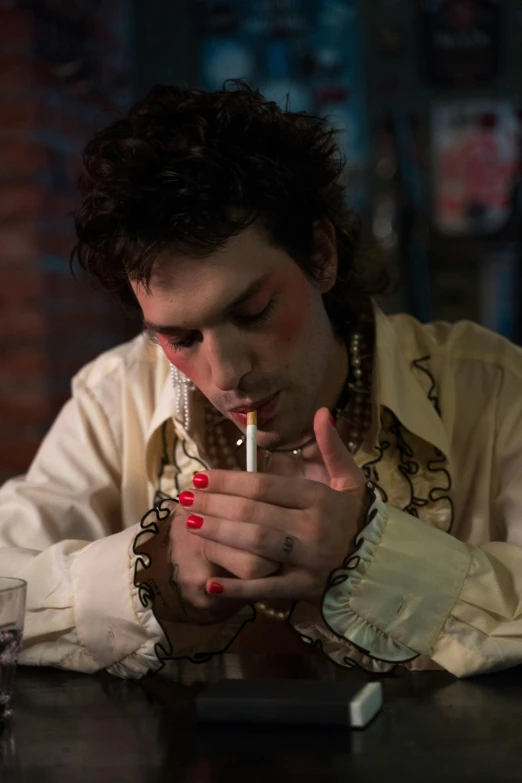 a man sitting at a table smoking a cigarette, an album cover, inspired by Nan Goldin, unsplash, renaissance, drag, [ theatrical ], jimi hendrix, travis touchdown