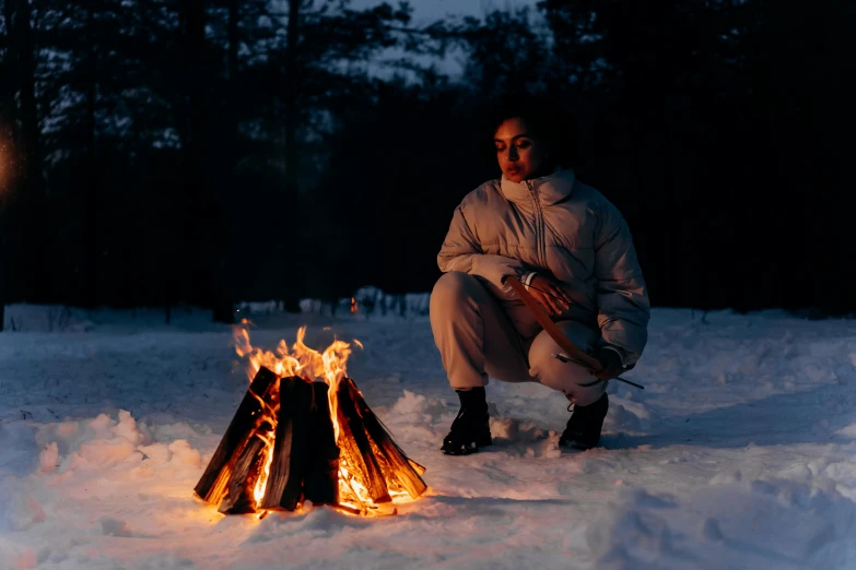 a man kneeling next to a fire in the snow, by Julia Pishtar, pexels contest winner, photograph of a techwear woman, s'mores, marina abramovic, evening lighting