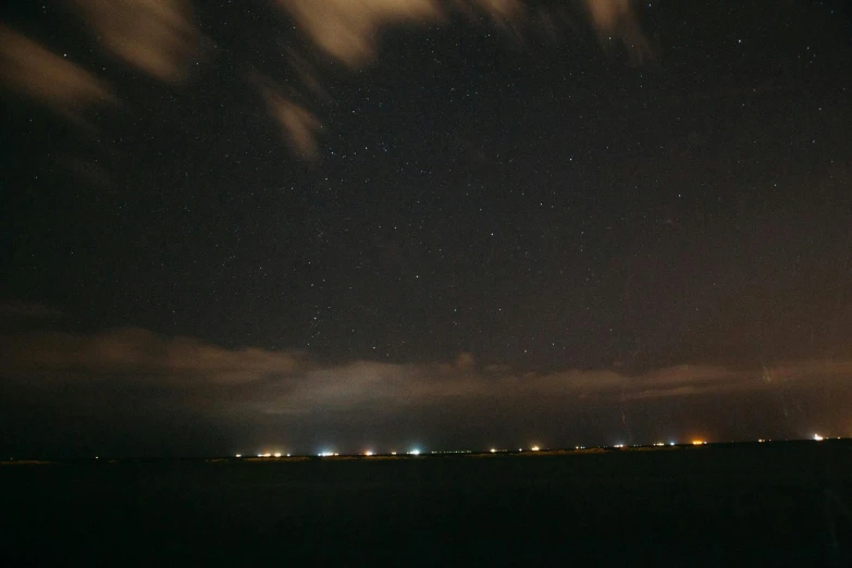 the night sky is full of stars and clouds, a portrait, pexels, light and space, the sea seen behind the city, mid shot photo, overcast skies, shot with a camera flash