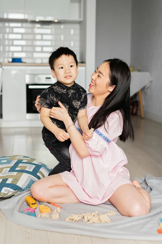 a woman sitting on the floor holding a baby, inspired by Cui Bai, pexels contest winner, wearing nanotech honeycomb robe, asian male, square, ikea