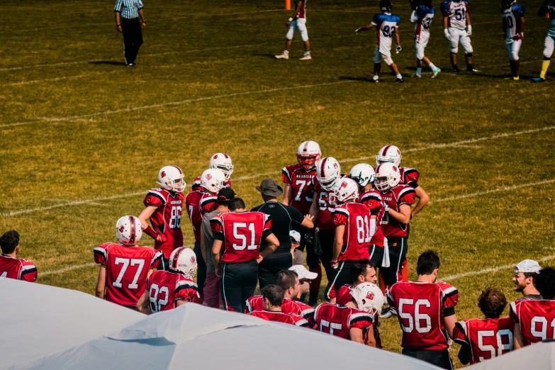 a group of football players standing on top of a field, by Arnie Swekel, pexels contest winner, red white and black, calmly conversing 8k, sumerville game, 2263539546]