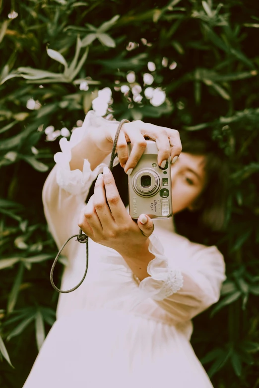 a woman taking a picture with a camera, inspired by Elsa Bleda, amongst foliage, on a pale background, photo product, an asian woman