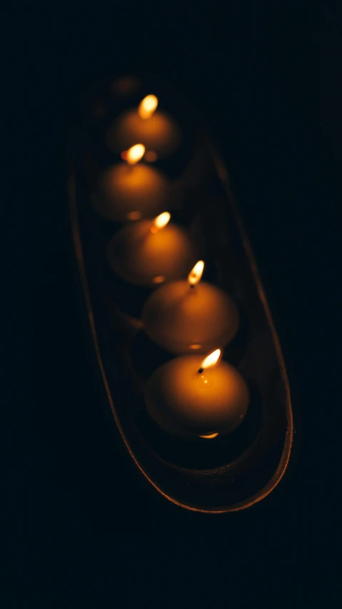 a row of lit candles in a dark room, an album cover, inspired by Elsa Bleda, trending on unsplash, minimalism, high angle close up shot, glowing orbs, high quality photo, on a wooden tray