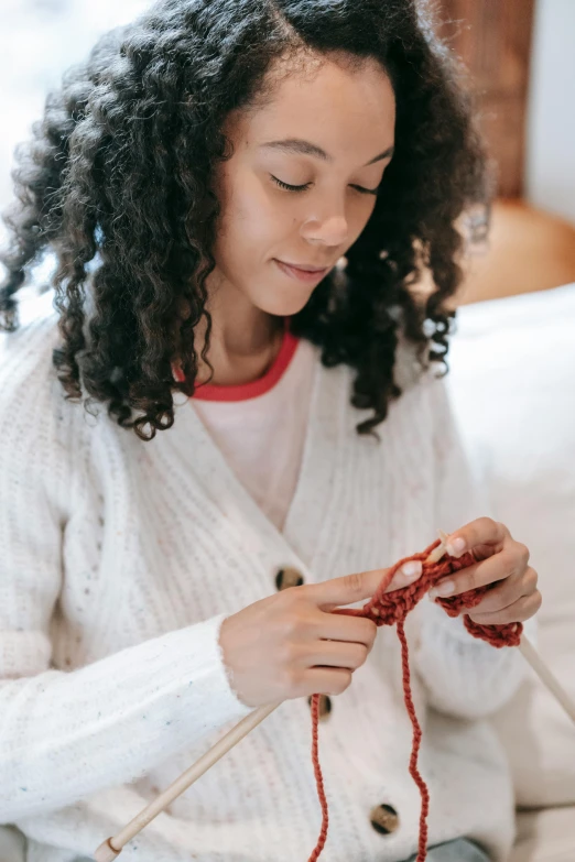 a woman sitting on a couch knitting a piece of yarn, trending on pexels, white and red color scheme, curls, teenage girl, wearing a white sweater