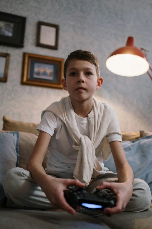 a young boy sitting on a couch playing a video game, by Adam Marczyński, pexels, hyperrealism, wearing a light shirt, portrait of tom holland, wearing white pajamas, gif