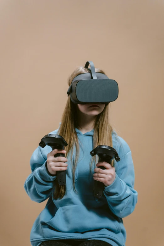 a woman in a blue sweatshirt holding two video game controllers, a hologram, trending on pexels, hypermodernism, oculus rift, avatar image, farming, dark. no text