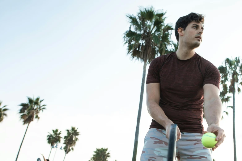 a man holding a tennis ball and racquet, an album cover, by Adam Dario Keel, standing near the beach, wearing a muscle tee shirt, flume, meet the actor behind the scenes