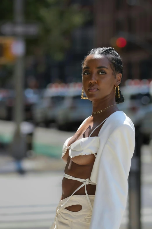 a woman standing on the side of a street, wearing a cropped tops, brown skinned, white bra, sharply focused